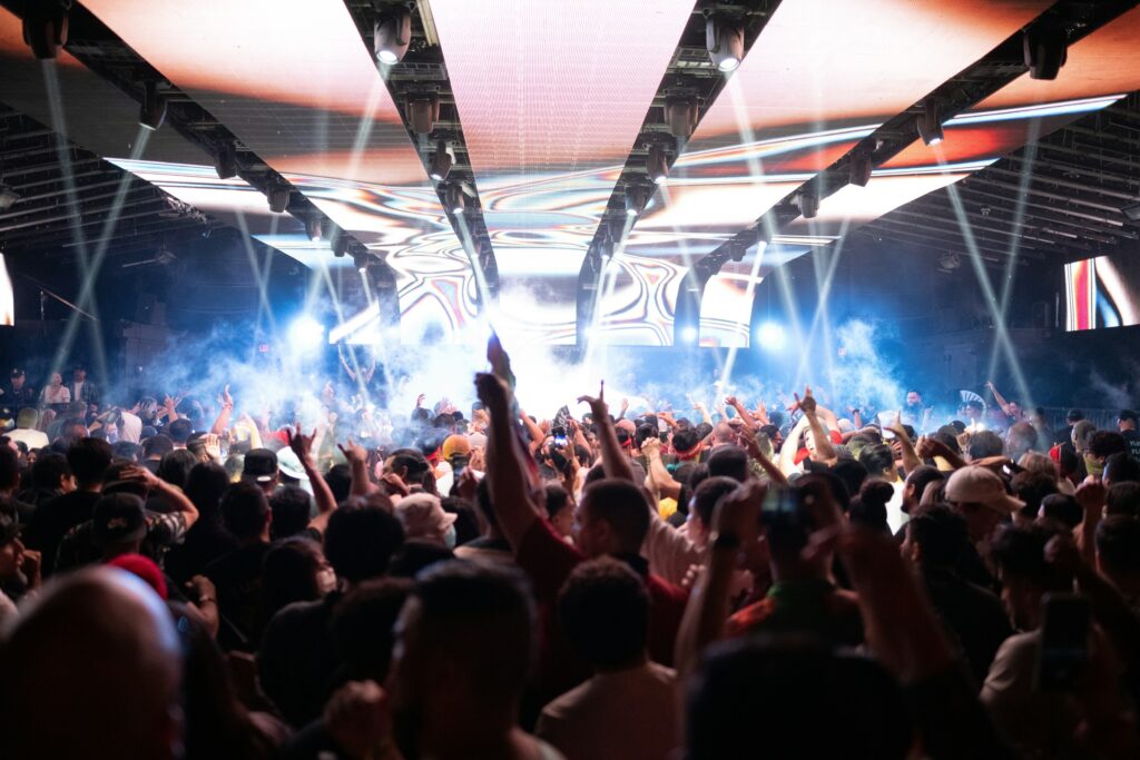 A large crowd watching a concert under coloured lights.