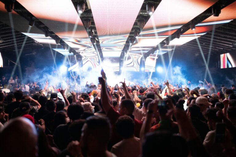 A large crowd watching a concert under coloured lights.