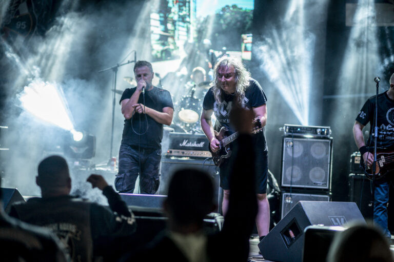 A live band performing for an energetic outdoor concert crowd at night.