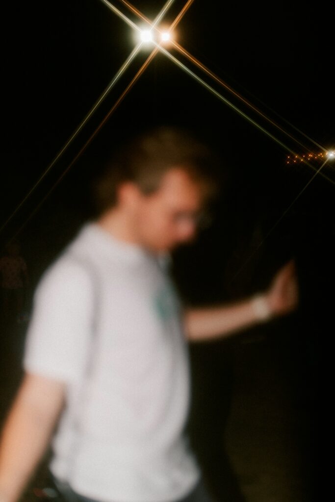 A person dancing at night among blurred red and purple lights.