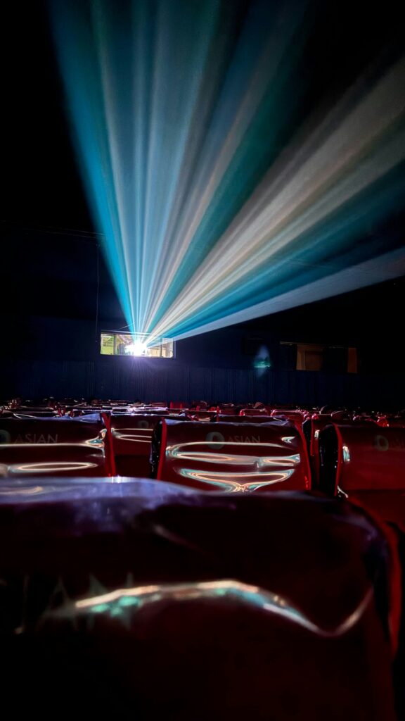 Projector beams crossing an empty cinema auditorium with red seats.