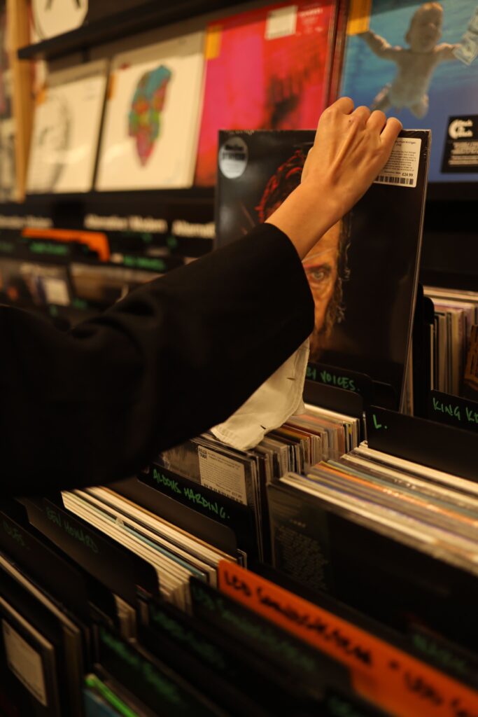 A hand choosing a vinyl record from a store shelf.